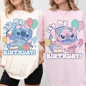 May include: Two t-shirts, one cream and one pink, featuring a cartoon character holding a cupcake, cake, and balloons. The text "It's My Birthday!" is printed below the character in a playful font. The shirts are casual and comfortable.