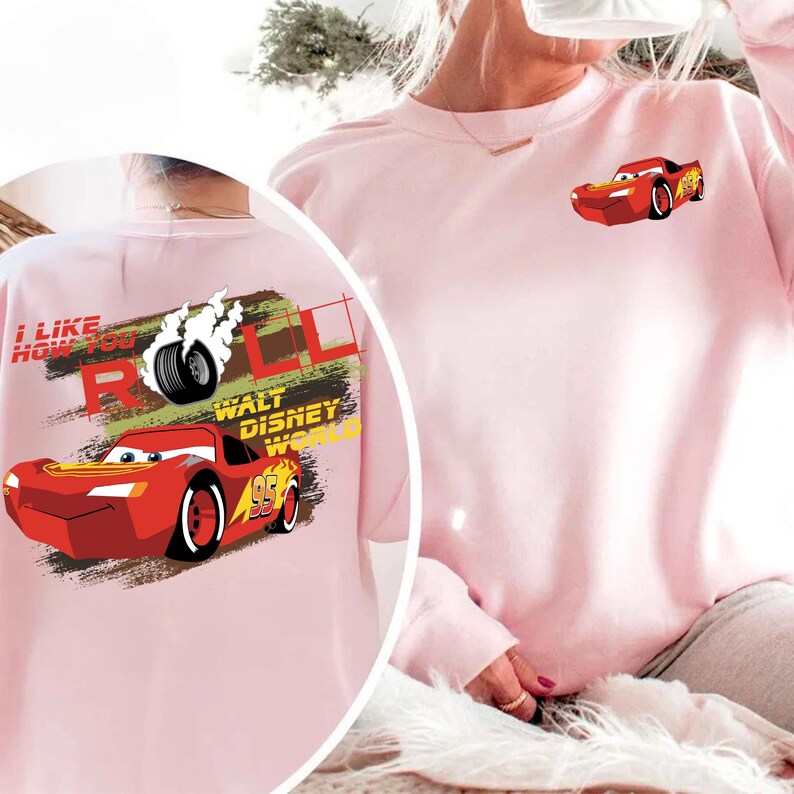 Puede incluir: Sudadera rosa claro con un dise&ntilde;o de Rayo McQueen de la pel&iacute;cula de Disney Cars. El dise&ntilde;o incluye el texto "I Like How You Roll" y "Walt Disney World". Una versi&oacute;n m&aacute;s peque&ntilde;a del coche est&aacute; en el pecho.