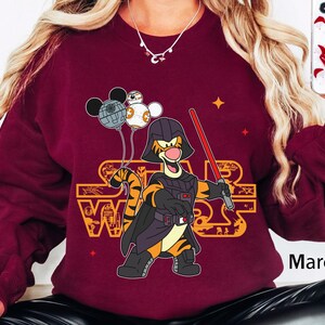 May include: A maroon sweatshirt with a graphic of Tigger from Winnie the Pooh dressed as Darth Vader from Star Wars. The graphic includes the text "Star Wars" and Mickey Mouse balloons.