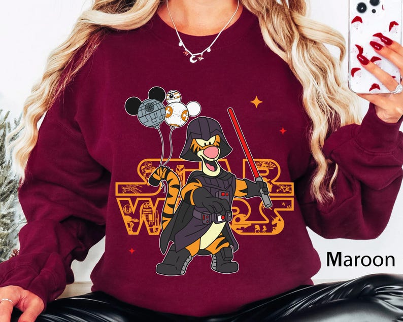 May include: A maroon sweatshirt with a graphic of Tigger from Winnie the Pooh dressed as Darth Vader from Star Wars. The graphic includes the text "Star Wars" and Mickey Mouse balloons.