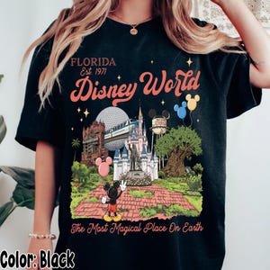 Puede incluir: Camiseta negra con un gr&aacute;fico colorido de Disney World. El dise&ntilde;o incluye el texto "FLORIDA Est. 1971 Disney World" y una representaci&oacute;n de los puntos de referencia del parque, incluido Mickey Mouse. Tambi&eacute;n aparece la frase "The Most Magical Place On Earth".