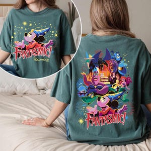 May include: Teal t-shirt with a front graphic of Mickey Mouse in a sorcerer's hat and the text "Fantasmic! Hollywood." The back showcases a colourful illustration of Disney characters, including Ursula and Ariel.