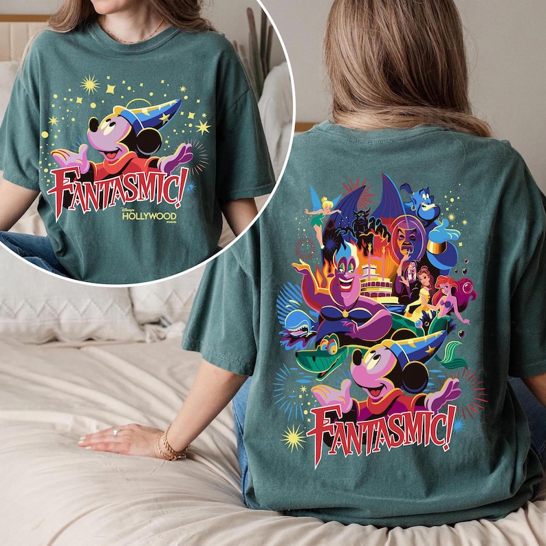 May include: Teal t-shirt with a front graphic of Mickey Mouse in a sorcerer's hat and the text "Fantasmic! Hollywood." The back showcases a colourful illustration of Disney characters, including Ursula and Ariel.