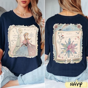 May include: Navy blue t-shirt featuring a front and back design. The front showcases Elsa and Anna from Frozen, while the back displays Olaf, snowflakes, and sheet music with the text "Let It Go".