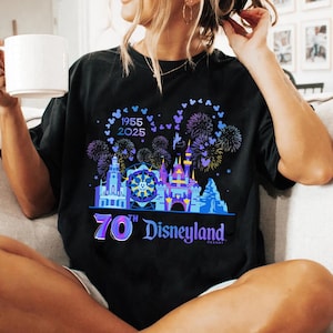 May include: Black t-shirt with a colorful graphic of Disneyland's 70th anniversary celebration. The graphic includes fireworks, Mickey Mouse silhouettes, and the Disneyland castle. The text "1955 2025 70th Disneyland Resort" is included in the graphic.