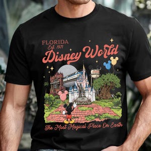 Puede incluir: Camiseta negra con un gr&aacute;fico colorido de Disney World. El dise&ntilde;o incluye el texto "Florida Est. 1971 Disney World" y una ilustraci&oacute;n de los puntos de referencia del parque, incluido Mickey Mouse. Tambi&eacute;n se incluye la frase "The Most Magical Place On Earth".