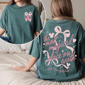 May include: Teal t-shirt with a pink castle and bow graphic on the front and the text "the most magical place on earth" on the back. The text includes Mickey Mouse silhouettes and stars.