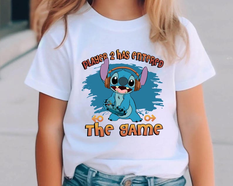 Puede incluir: Camiseta blanca con un personaje azul Stitch sosteniendo un mando de videojuego. El texto "Player 2 has entered the game" est&aacute; impreso en la camiseta.
