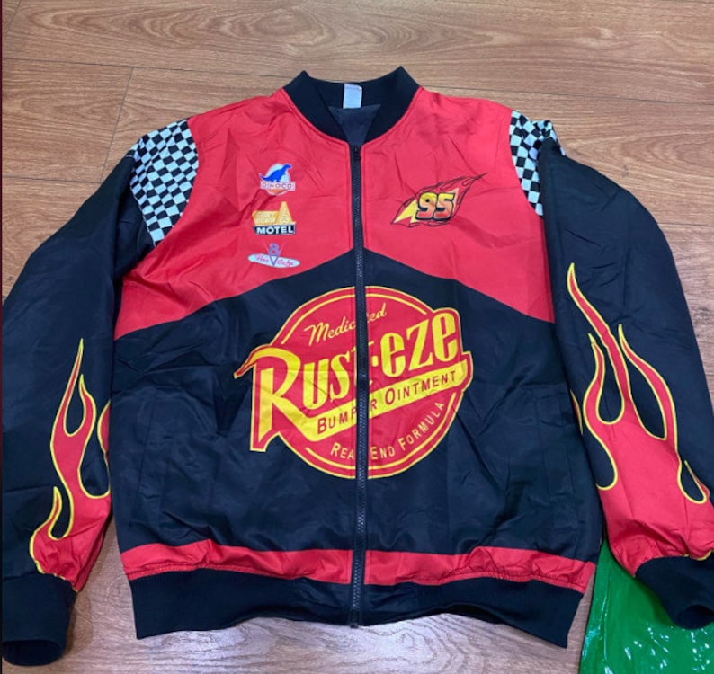 May include: A black and red bomber jacket with a checkered pattern on the sleeves. The jacket features a large Rust-eze logo with the text "Medicated Bumper Ointment" and "Real End Formula". The jacket also has a small "95" logo and a "Motel" logo.