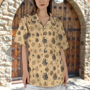 May include: A short-sleeved, button-down shirt in a tan color, featuring a repeating pattern of pirate-themed illustrations. The design includes skulls, crossed swords, anchors, and ships. The shirt has a classic collar and a relaxed fit.