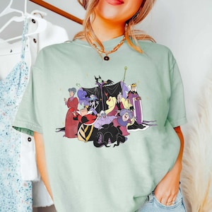 May include: A light green t-shirt with a graphic print of Disney villains. The villains include Maleficent, Ursula, Cruella de Vil, and the Evil Queen.