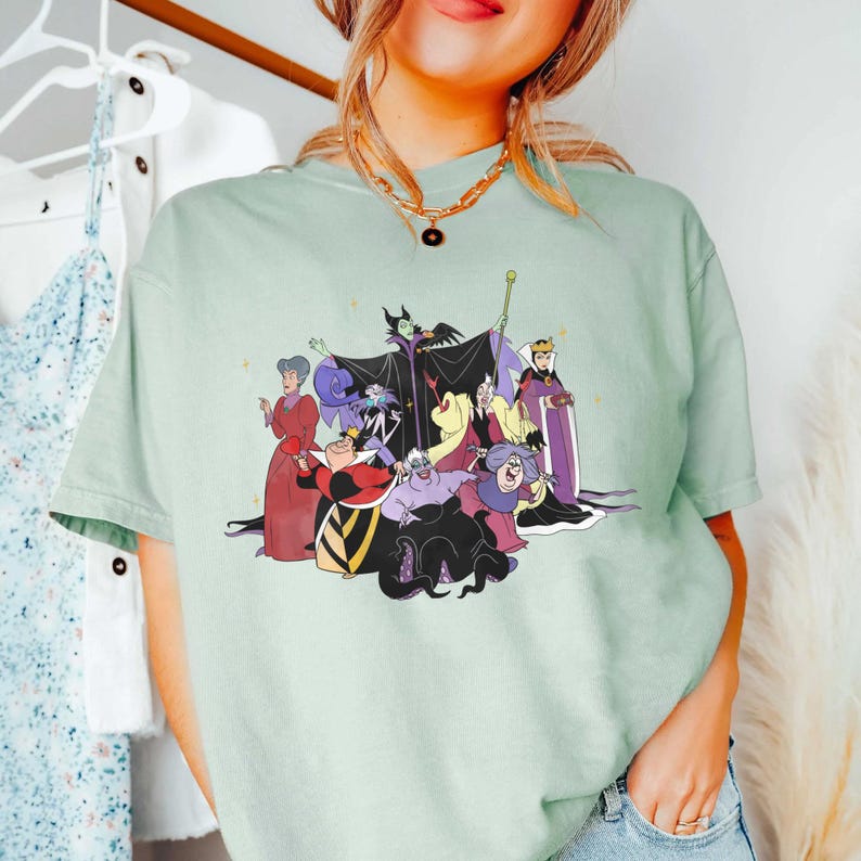 May include: A light green t-shirt with a graphic print of Disney villains. The villains include Maleficent, Ursula, Cruella de Vil, and the Evil Queen.