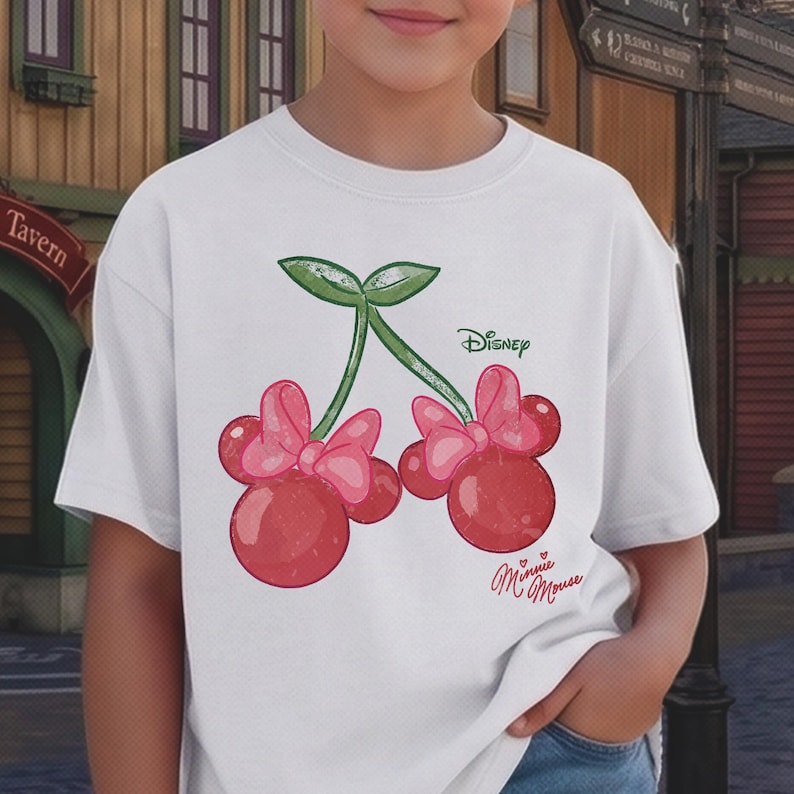 Op de afbeelding: Wit T-shirt met een grillig ontwerp van twee kersen met roze strikken, die lijken op de iconische look van Minnie Mouse. Het woord "Disney" staat boven de kersen gedrukt en "Minnie Mouse" staat eronder.