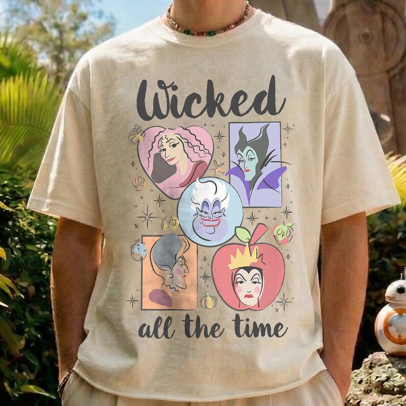 K&ouml;nnte beinhalten: Cremefarbenes T-Shirt mit dem Text "Wicked all the time" und Illustrationen von Zeichentrickfiguren. Das Design umfasst ein Herz, einen Apfel und andere Formen. Das Shirt hat kurze &Auml;rmel.