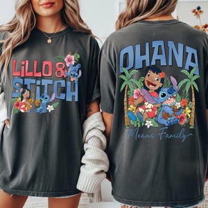 May include: Dark gray t-shirts featuring the characters Lilo and Stitch. The front of the shirt says "Lilo & Stitch" with images of the characters and flowers. The back of the shirt says "Ohana Means Family" with images of the characters and palm trees.