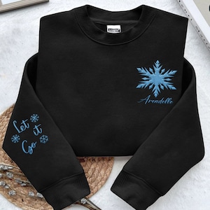 May include: Black sweatshirt with a blue snowflake and the text "Arendelle" embroidered on the front. The left sleeve has the text "Let it Go" and snowflakes embroidered on it.
