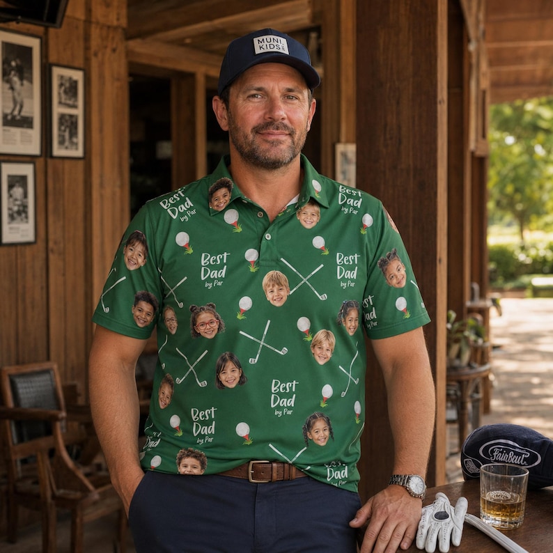 May include: A green polo shirt with a pattern of children's faces, golf balls, and crossed golf clubs. The text "Best Dad by Par" is repeated throughout the design. The man is wearing a navy blue cap with "Muni Kids" on it.
