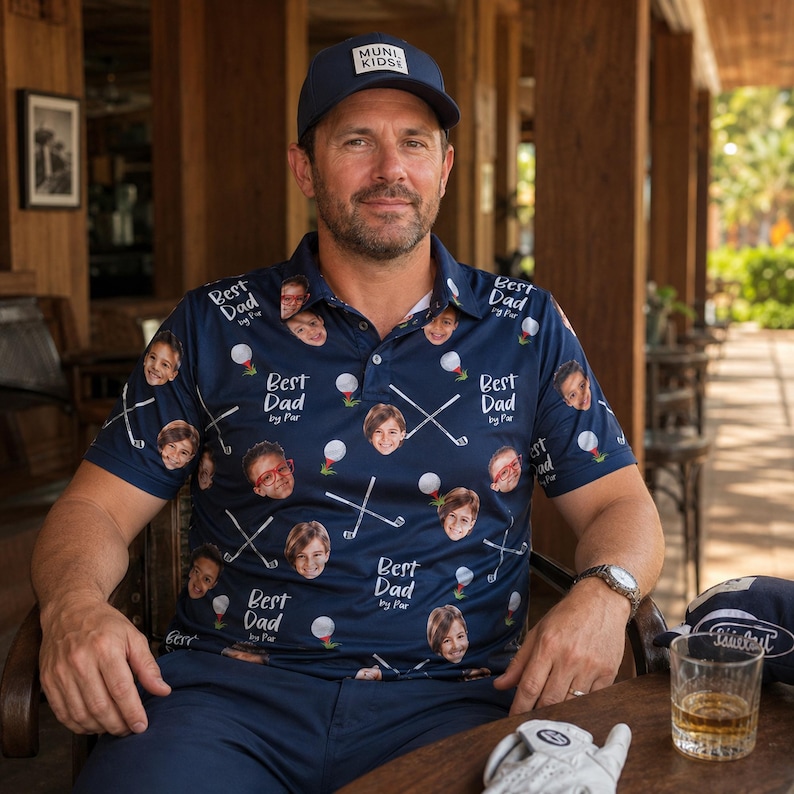 May include: A navy blue polo shirt with a pattern of children's faces, golf balls, and crossed golf clubs. The shirt has the text "Best Dad by Par" repeated throughout. A navy blue baseball cap with "MUNI KIDS" is also visible.