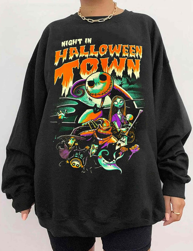 Może przedstawiać: Czarna bluza z nadrukiem graficznym postaci z filmu "Koszmar przed świętami". Na bluzce widnieje napis "Night in Halloween Town".