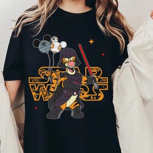 May include: Black t-shirt with a graphic of Tigger dressed as Darth Vader holding a lightsaber. Tigger is holding a Death Star, a TIE fighter, and a Stormtrooper helmet. The text "Star Wars" is printed in orange on the shirt.