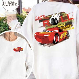 Puede incluir: Sudadera blanca con un dise&ntilde;o de coche de carreras rojo de dibujos animados. El texto dice "I LIKE HOW YOU ROLL" y "WALT DISNEY WORLD". El dise&ntilde;o incluye un neum&aacute;tico con humo y el n&uacute;mero 95.