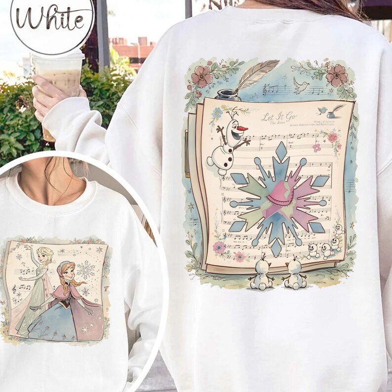 May include: White sweatshirt featuring a colorful illustration from the movie "Frozen." The design includes musical notes, snowflakes, and characters like Olaf and Elsa. The text "Let It Go" is visible on the sheet music.