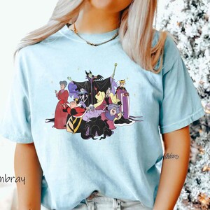May include: A light blue t-shirt with a graphic print of Disney villains, including Maleficent, Ursula, Cruella de Vil, and the Evil Queen. The villains are depicted in a group, with Maleficent in the center.