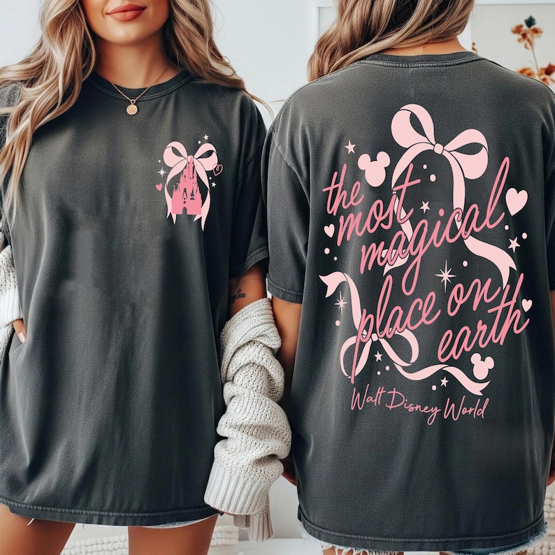 May include: Dark gray t-shirts with pink graphics. One shirt features a castle and bow design, the other says "the most magical place on earth" with a bow, stars, and Mickey Mouse icons. Walt Disney World is also printed.