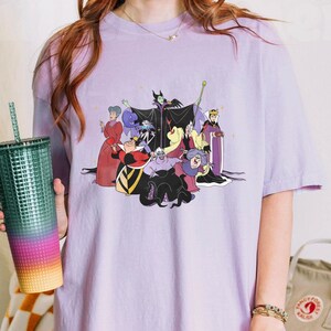 May include: A purple t-shirt with a graphic print of Disney villains, including Maleficent, Ursula, Cruella de Vil, and the Evil Queen. The villains are depicted in a group, with Maleficent in the center.