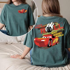 Puede incluir: Camiseta de color verde azulado con un dise&ntilde;o de coche de carreras rojo de dibujos animados en la parte delantera y trasera. El dise&ntilde;o trasero incluye el texto "I LIKE HOW YOU ROLL" y "WALT DISNEY WORLD". El coche tiene el n&uacute;mero 95.