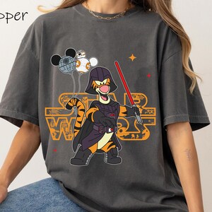 May include: A gray t-shirt with a cartoon image of Tigger dressed as Darth Vader holding a lightsaber. Tigger is holding balloons that look like the Death Star and other Star Wars characters. The text "Star Wars" is printed on the shirt.