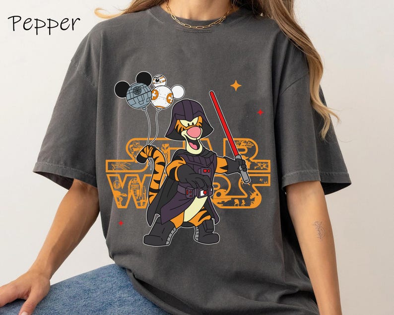 May include: A gray t-shirt with a cartoon image of Tigger dressed as Darth Vader holding a lightsaber. Tigger is holding balloons that look like the Death Star and other Star Wars characters. The text "Star Wars" is printed on the shirt.