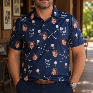 May include: Navy blue polo shirt with a golf-themed pattern featuring golf balls, crossed golf clubs, and children's faces. The shirt has the text "Best Dad by Par" repeated throughout the design.