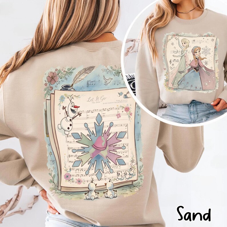 May include: Sand-colored sweatshirt featuring a musical score design with the text "Let It Go" and illustrations of Olaf and snowflakes. The sweatshirt also has a circular image of two characters from the movie. A cozy and stylish top.