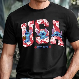 May include: Black t-shirt featuring the word "USA" in a red floral pattern with three cartoon characters. The text "EST. 1776" is below the word "USA". The characters are blue with large eyes.