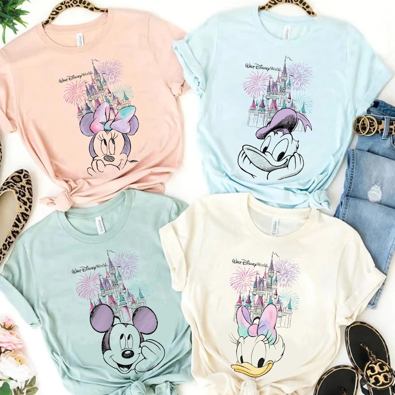 Pode incluir: Quatro camisetas em tons pastel com personagens da Disney e o texto "Walt Disney World". Cada camisa exibe um personagem diferente: Minnie Mouse, Pato Donald, Mickey Mouse e Margarida, com um castelo e fogos de artif&iacute;cio.