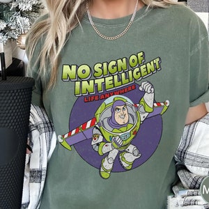 May include: Green t-shirt with a distressed look featuring a cartoon image of Buzz Lightyear from the Toy Story movie franchise. The text on the shirt reads "No Sign of Intelligent Life Anywhere".