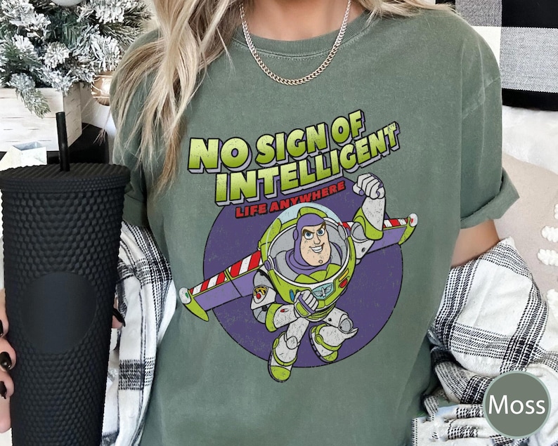 May include: Green t-shirt with a distressed look featuring a cartoon image of Buzz Lightyear from the Toy Story movie franchise. The text on the shirt reads "No Sign of Intelligent Life Anywhere".