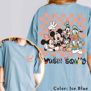 May include: Pale blue t-shirt with a graphic of Mickey Mouse, Minnie Mouse, Goofy, Donald Duck, and Daisy Duck. The back has a checkered pattern with stars and the words "Mousin' Squad". The front has a small graphic of Stitch.