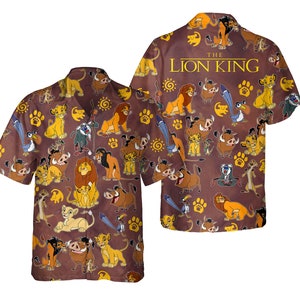 Puede incluir: Una camisa de manga corta con botones de color marrón con un patrón repetido de personajes de El Rey León. La camisa presenta a Simba, Nala, Timon, Pumbaa, Scar y otros personajes de la película. El texto "The Lion King" está impreso en la camisa.