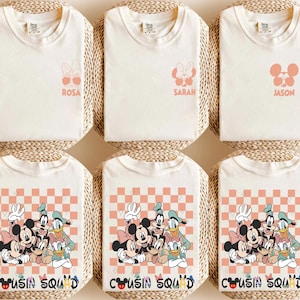 May include: Six cream-coloured t-shirts. The top row features shirts with character graphics and names: Rosa, Sarah, and Jason. The bottom row has shirts with a graphic of Mickey Mouse, Minnie Mouse, Donald Duck, and Goofy, with the text "Cousin Squad".