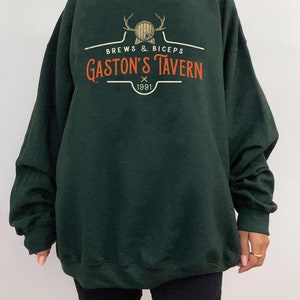 Op de afbeelding: Forestgroen Gildan sweatshirt met een vintage-stijl logo met de tekst "Brews & Biceps Gaston's Tavern 1991".