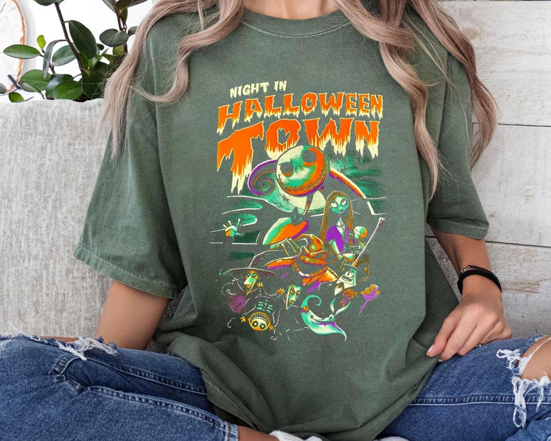 Może przedstawiać: Zielona koszulka z nadrukiem graficznym postaci z filmu "Koszmar przed świętami". Na koszulce widnieje napis "Night in Halloween Town".