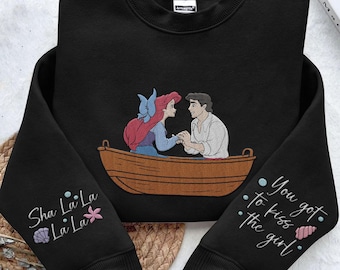 May include: Black sweatshirt with a graphic of Ariel and Prince Eric from The Little Mermaid in a boat. The text "Sha La La La La La" is on one sleeve and "You got to kiss the girl" is on the other sleeve.