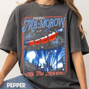 Könnte beinhalten: Dunkelgraues T-Shirt mit einem grafischen Design. Das Design zeigt den Text "Paging Mr. Morrow" in Blau und Rot, eine Raketenillustration und Feuerwerk. Das Wort "Pepper" ist unten aufgedruckt.