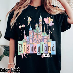 Puede incluir: Camiseta negra con un gr&aacute;fico del castillo de Disneyland en colores pastel, Campanilla, globos de Mickey Mouse y la palabra "Disneyland". El dise&ntilde;o incluye estrellas.