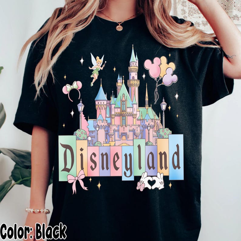 Puede incluir: Camiseta negra con un gr&aacute;fico del castillo de Disneyland en colores pastel, Campanilla, globos de Mickey Mouse y la palabra "Disneyland". El dise&ntilde;o incluye estrellas.