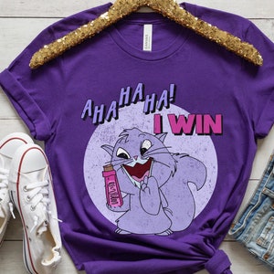 Puede incluir: Camiseta morada con un gato de dibujos animados sosteniendo una barra de caramelo rosa y blanca. El gato es morado y tiene la nariz y la lengua rosas. El texto de la camiseta dice "AHA HA HA! I WIN".