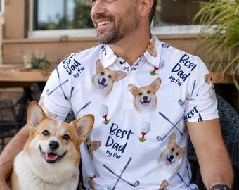 May include: White polo shirt featuring a pattern of corgi dogs, golf clubs, and golf balls. The shirt has the text "Best Dad by Par". A corgi dog is sitting next to a person wearing the shirt.