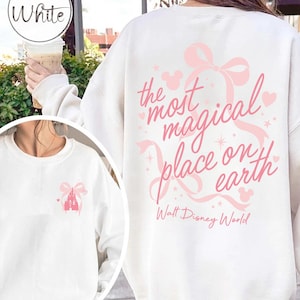 May include: White sweatshirt with a pink bow and the text "the most magical place on earth" in pink script. The sweatshirt also features a pink castle graphic and the words "Walt Disney World".